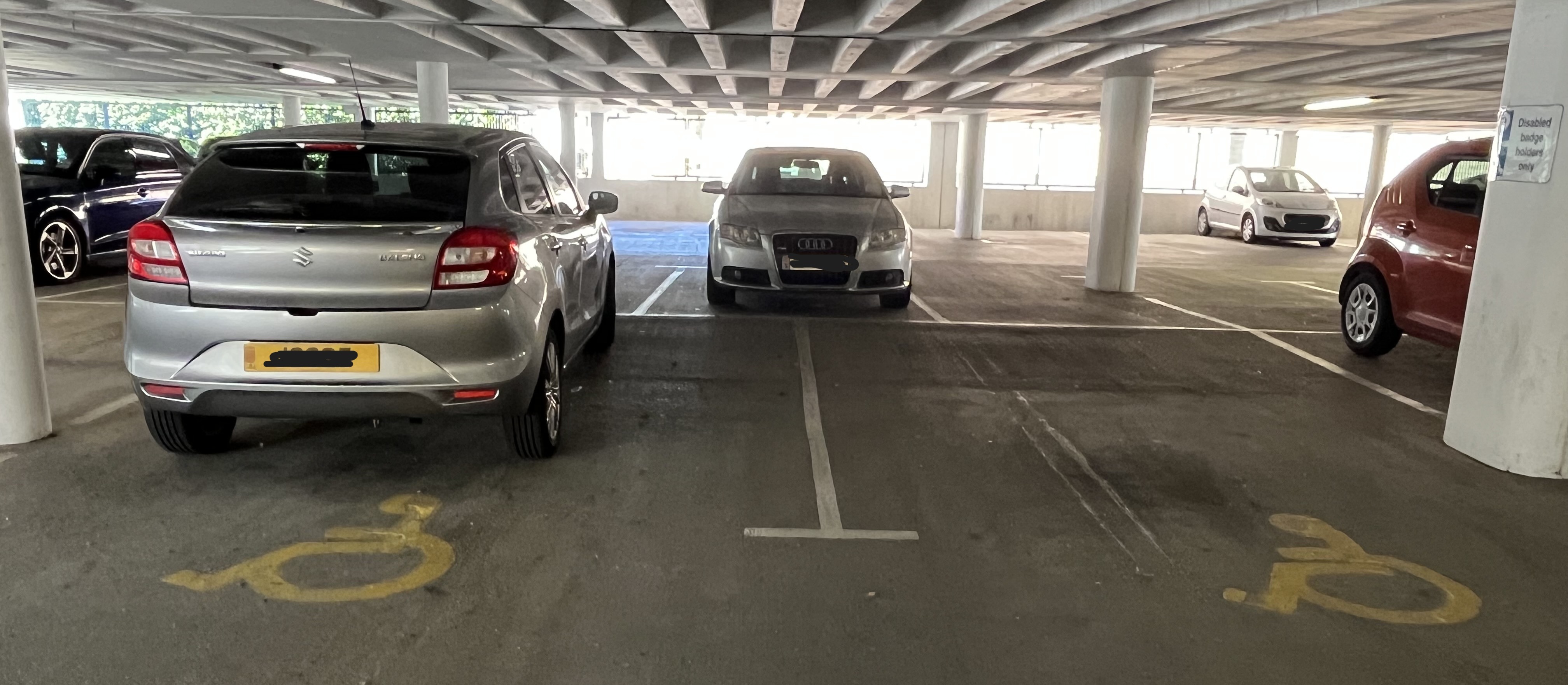 Covered car park with marked disabled parking bays, support columns, and several parked cars under a concrete ceiling.